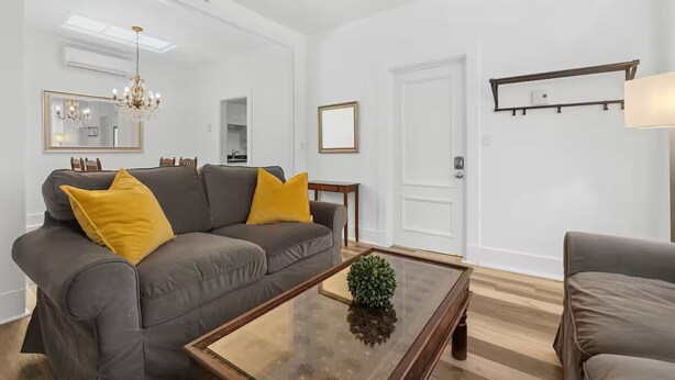 A modern living room with a grey sofa, yellow cushions, a glass coffee table, and a chandelier. - Perfect Location! Perfect Stay in Québec City! Suite Belle (Québec)
