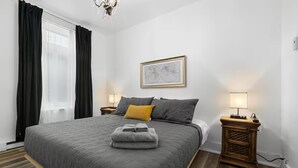 A modern bedroom with a large bed, two bedside tables, a nightstand, a chandelier, and a framed picture on the wall. - Perfect Location! Perfect Stay in Québec City! Suite Belle (Québec)