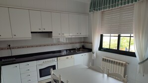 Een keuken met witte kastjes, een zwart aanrecht, een witte tafel en een raam met zonwering.