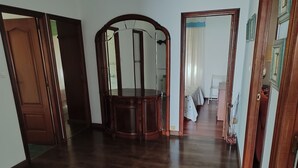 Een ruime kamer met een gepolijste houten vloer, een grote houten kast en een spiegel met een gebogen bovenkant.