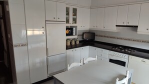 Een keuken met witte kasten, een fornuis, een magnetron en een eettafel met stoelen.