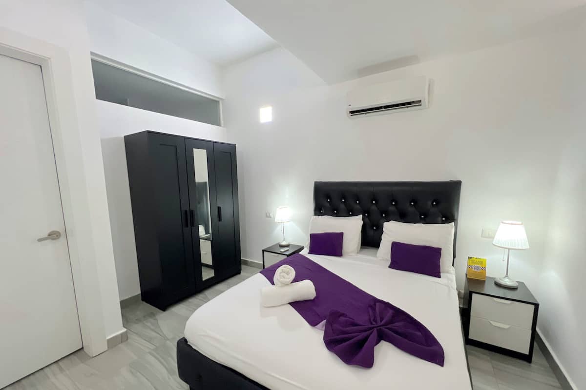 A neatly arranged bedroom with a bed, bedside tables, a wardrobe, and an air conditioning unit.