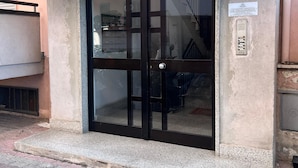 Entrada d'un edifici amb una porta de vidre, una nansa de metall i un petit cartell a la paret.