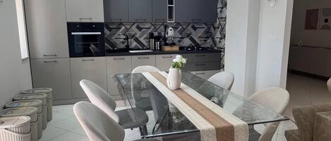 Un comedor moderno con una mesa de vidrio, sillas acolchadas y una cocina contemporánea al fondo.