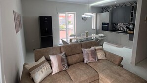 Sala de estar moderna com um amplo sofá em formato de L, área de cozinha com mesa de jantar e vista para a varanda.