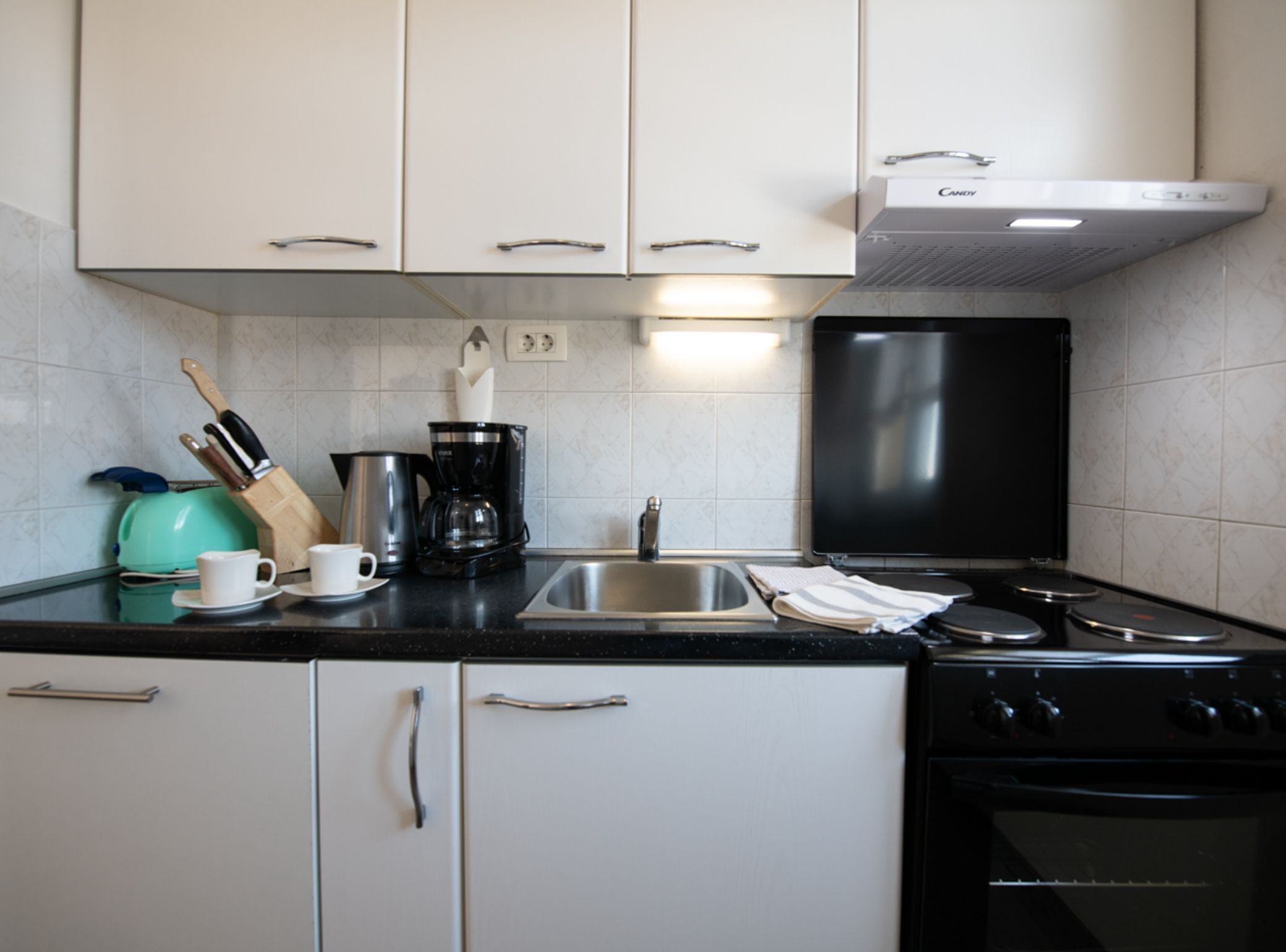 A kitchen with white cabinets, a black stove, a sink, and a coffee maker.