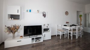 A modern living room with a flat-screen TV, white furniture, a dining area with a table and chairs, and a decorative wall piece. - Apartments Mirjana IKA (Ika)