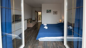 A bedroom with a bed, a sofa, a TV, and a bathroom visible through a glass door. - Apartments Mirjana IKA (Ika)
