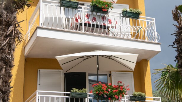 A yellow building with a balcony featuring white railings, potted plants, and a table with chairs. - Apartments Mirjana IKA (Ika)