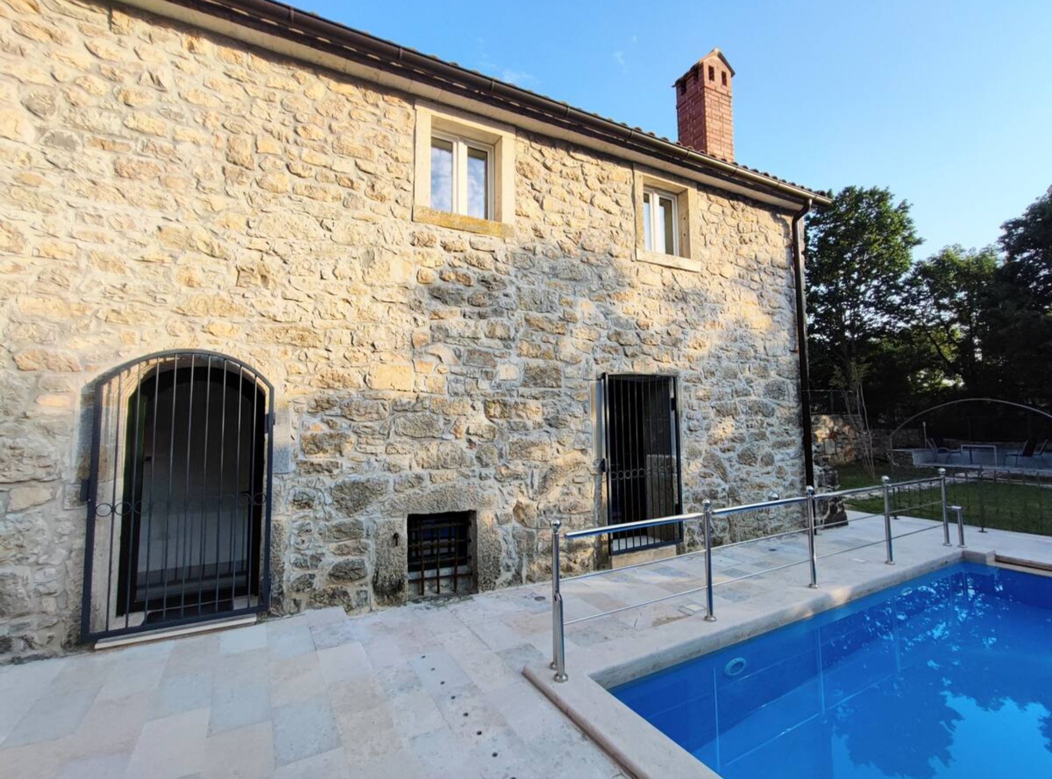 A stone building with a swimming pool, featuring arched windows and a chimney.