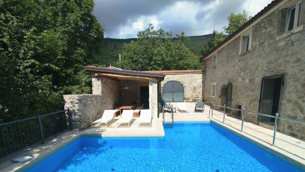 A swimming pool with lounge chairs, a stone building, and a stone wall.