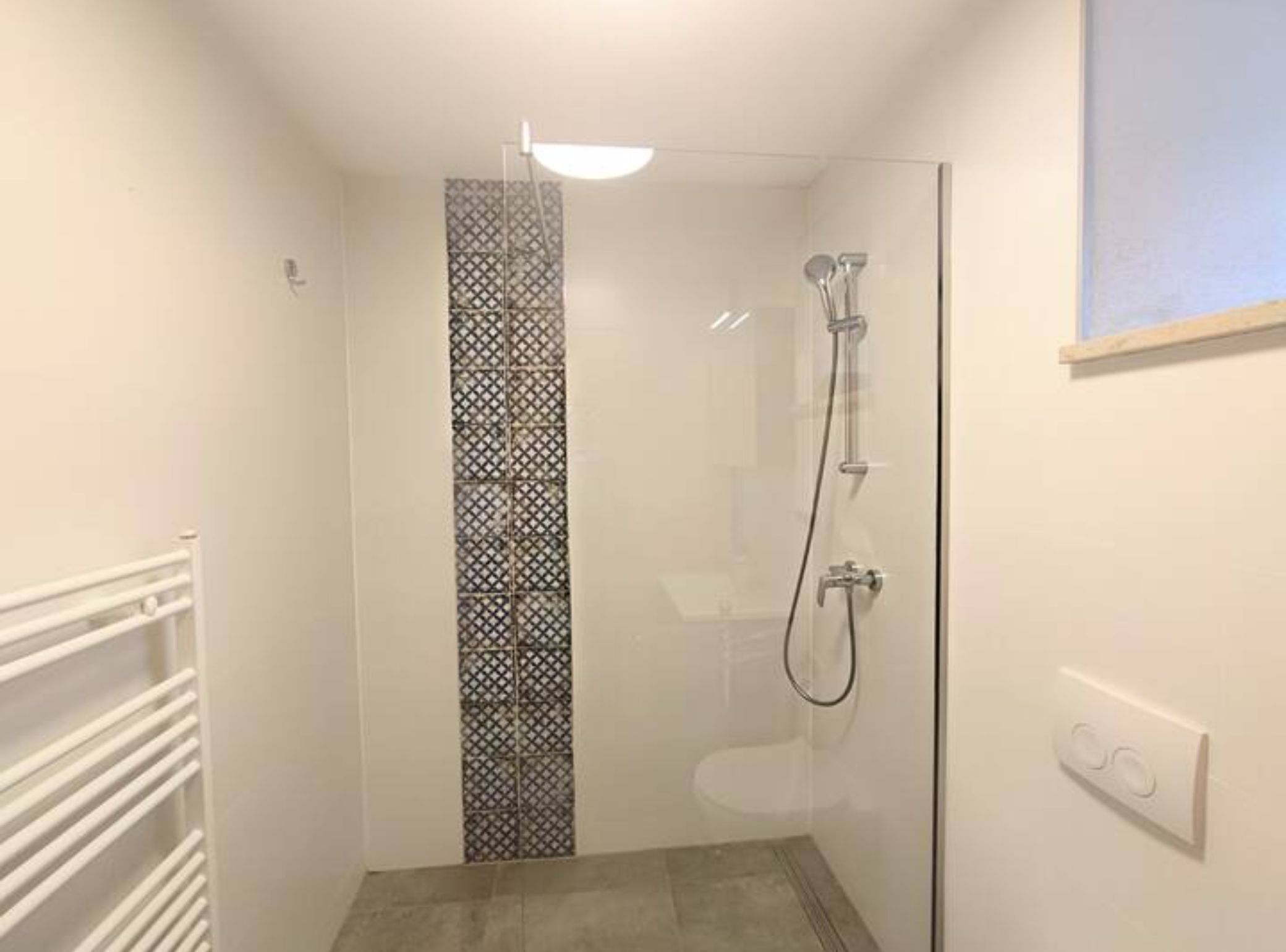 Et lille, lukket bruseområde med glasdør, brusehoved og kontrolpanel på væggen.