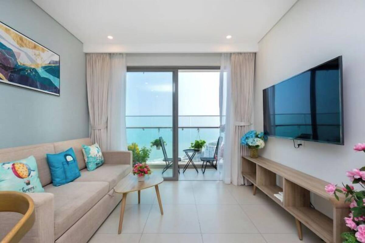 Ein modernes Wohnzimmer mit Sofa, Couchtisch, Fernseher und Balkon mit Pflanzen.