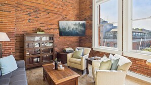 A cozy living room with a brick wall, a large window, a sofa, a coffee table, and a cabinet. - High Ceilings and Modern Loft Living (Victoria Central British Columbia Provincial Government)
