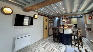 A modern kitchen with a central island, wooden beams, and a flat-screen TV mounted on the wall. - Riva Bella Marine (Ouistreham)