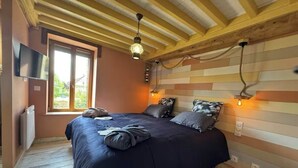 A bedroom with a bed, wooden ceiling beams, a window, and a wall-mounted TV. - Riva Bella Marine (Ouistreham)