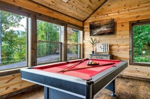 A pool table in a room with wooden walls and large windows.