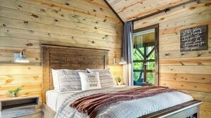 A wooden cabin bedroom with a bed, two bedside tables, a window, and a motivational quote on the wall. - 3 BR • Hot tub • Game Room • Mtn Views • Pools • Golf (Gatlinburg)