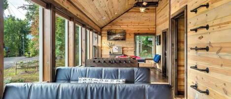 Interior de una cabaña con una larga mesa de comedor, asientos de cuero y paredes de madera.