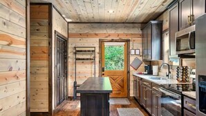 A compact kitchen with wooden walls, a central island, dark cabinets, and a view of greenery outside. - 3 BR • Hot tub • Game Room • Mtn Views • Pools • Golf (Gatlinburg)