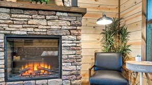 A stone fireplace with a glass front, a black leather chair, and a small table with a lamp. - 3 BR • Hot tub • Game Room • Mtn Views • Pools • Golf (Gatlinburg)