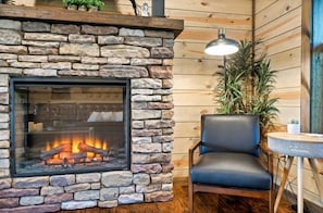 A stone fireplace with a glass front, a black leather chair, and a small table with a lamp. - 3 BR • Hot tub • Game Room • Mtn Views • Pools • Golf (Gatlinburg)