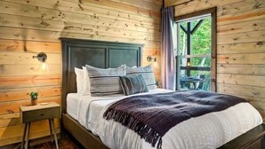 A wooden-paneled bedroom with a bed, bedside table, and a window with a view of greenery. - 3 BR • Hot tub • Game Room • Mtn Views • Pools • Golf (Gatlinburg)