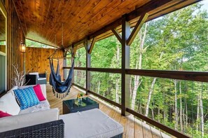 Una terraza de madera con una hamaca, un sofá con cojines de colores y una mesa con un jarrón.