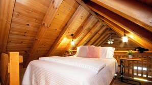 Una camera da letto mansardata accogliente con soffitto in legno, un letto grande con biancheria bianca e un tavolino con una pianta.