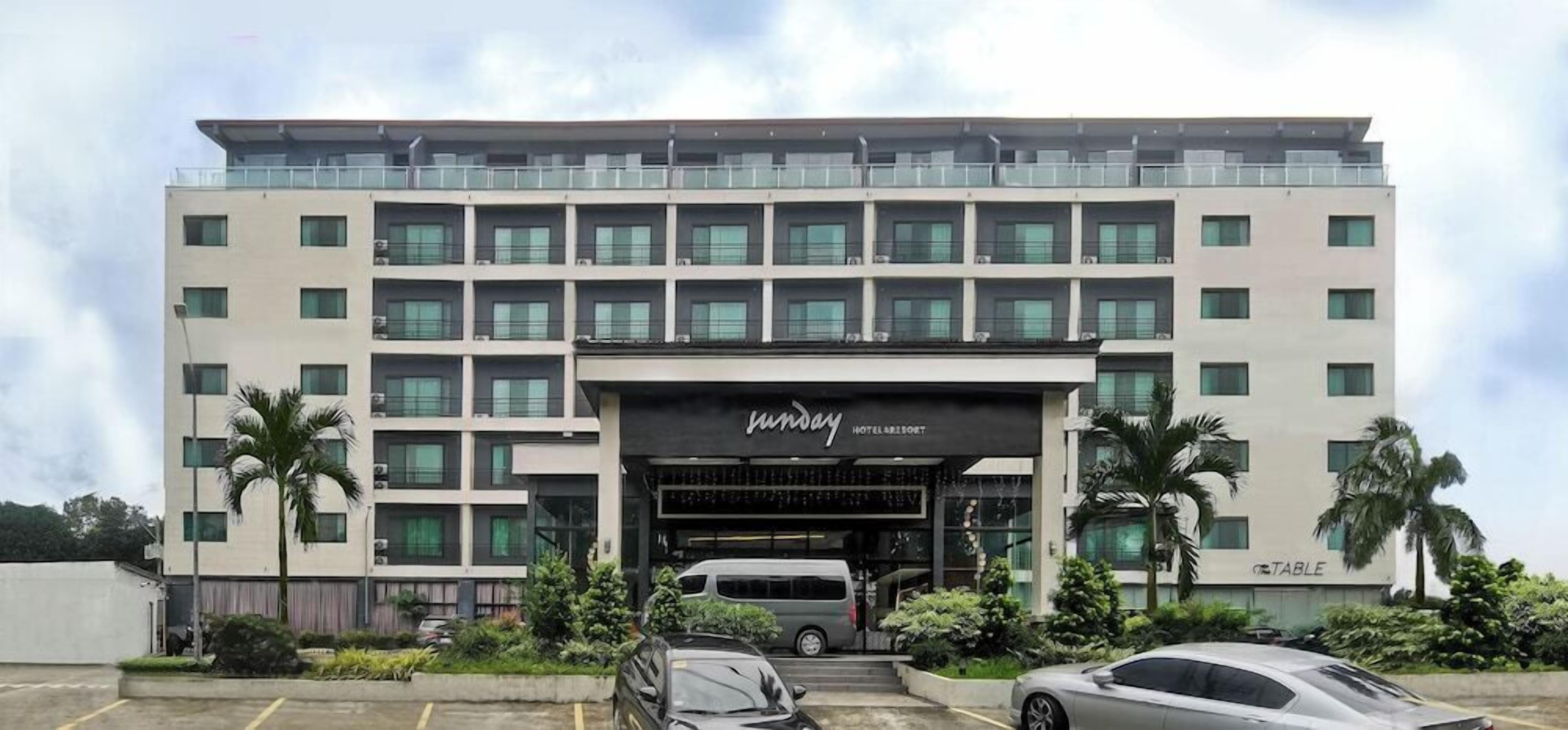 Um hotel de vários andares com fachada moderna, entrada coberta e área de estacionamento com carros.