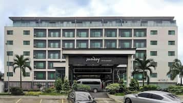 Um hotel de vários andares com fachada moderna, entrada coberta e área de estacionamento com carros.