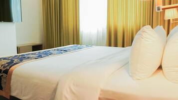 A hotel room with a bed, a TV mounted on the wall, and a lamp on the bedside table.
