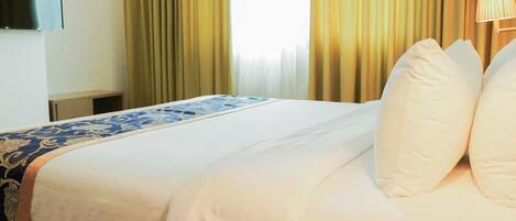 A hotel room with a bed, a TV mounted on the wall, and a lamp on the bedside table.