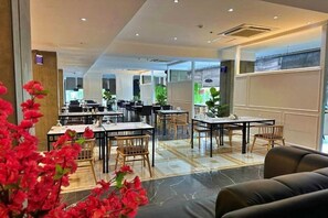 Eine Hotelhalle mit mehreren Esstischen, Stühlen und einer Sitzecke.