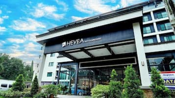 A modern hotel building with a prominent entrance, glass facade, and signage for 'HEVEA HOTEL & RESORT.'