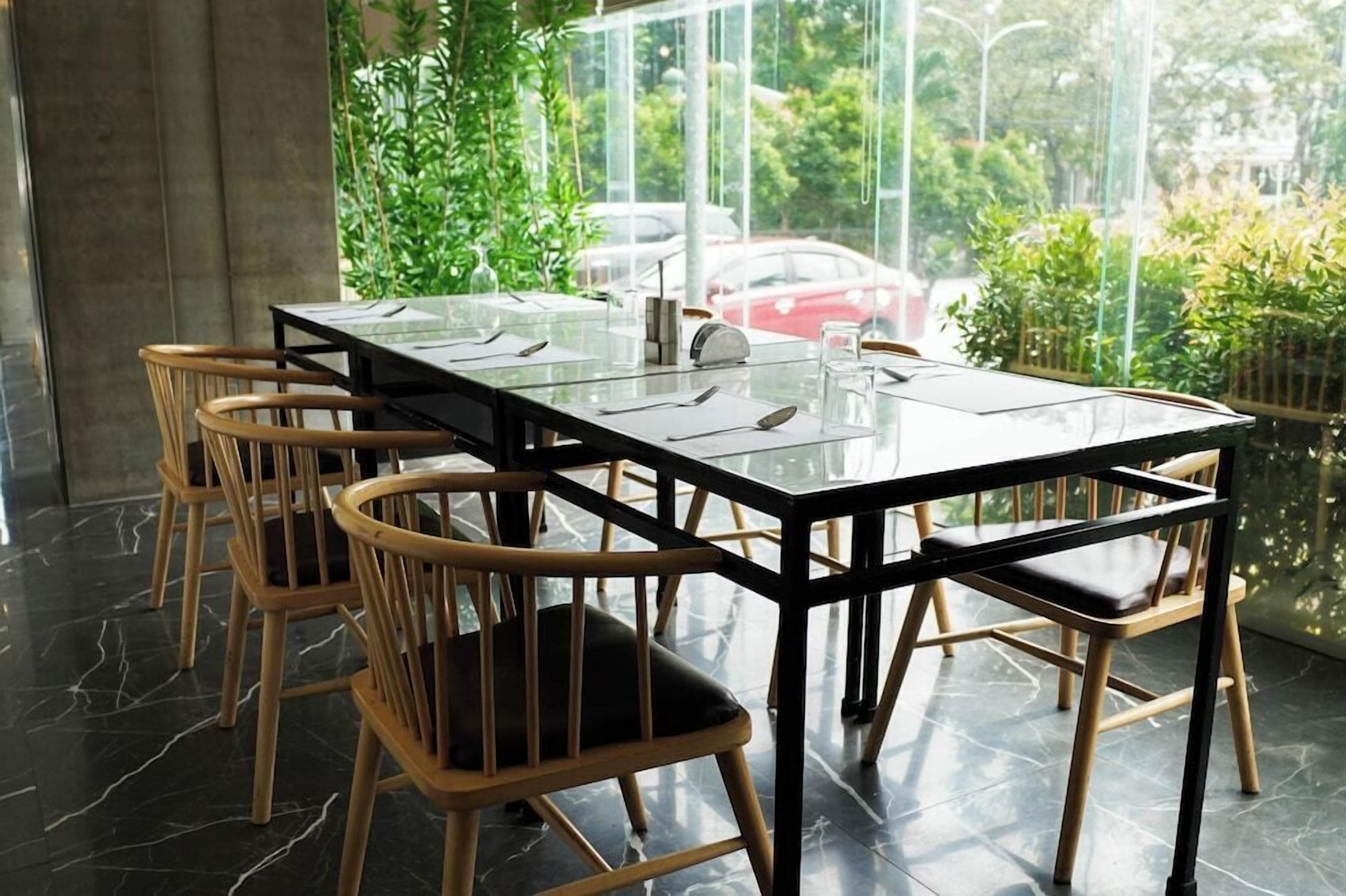 A dining area with a glass-top table, wooden chairs, and a view of greenery and parked cars.