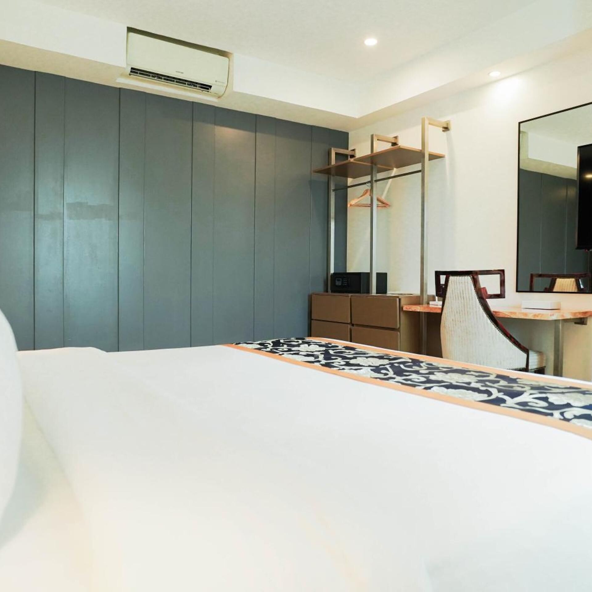 Quarto de hotel com cama, escrivaninha, cadeira, cômoda, espelho e ar condicionado.