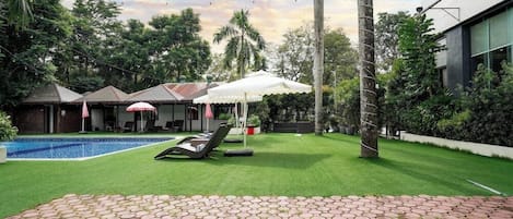 A pool area with a lounge chair, a covered seating area, and a well-maintained lawn.