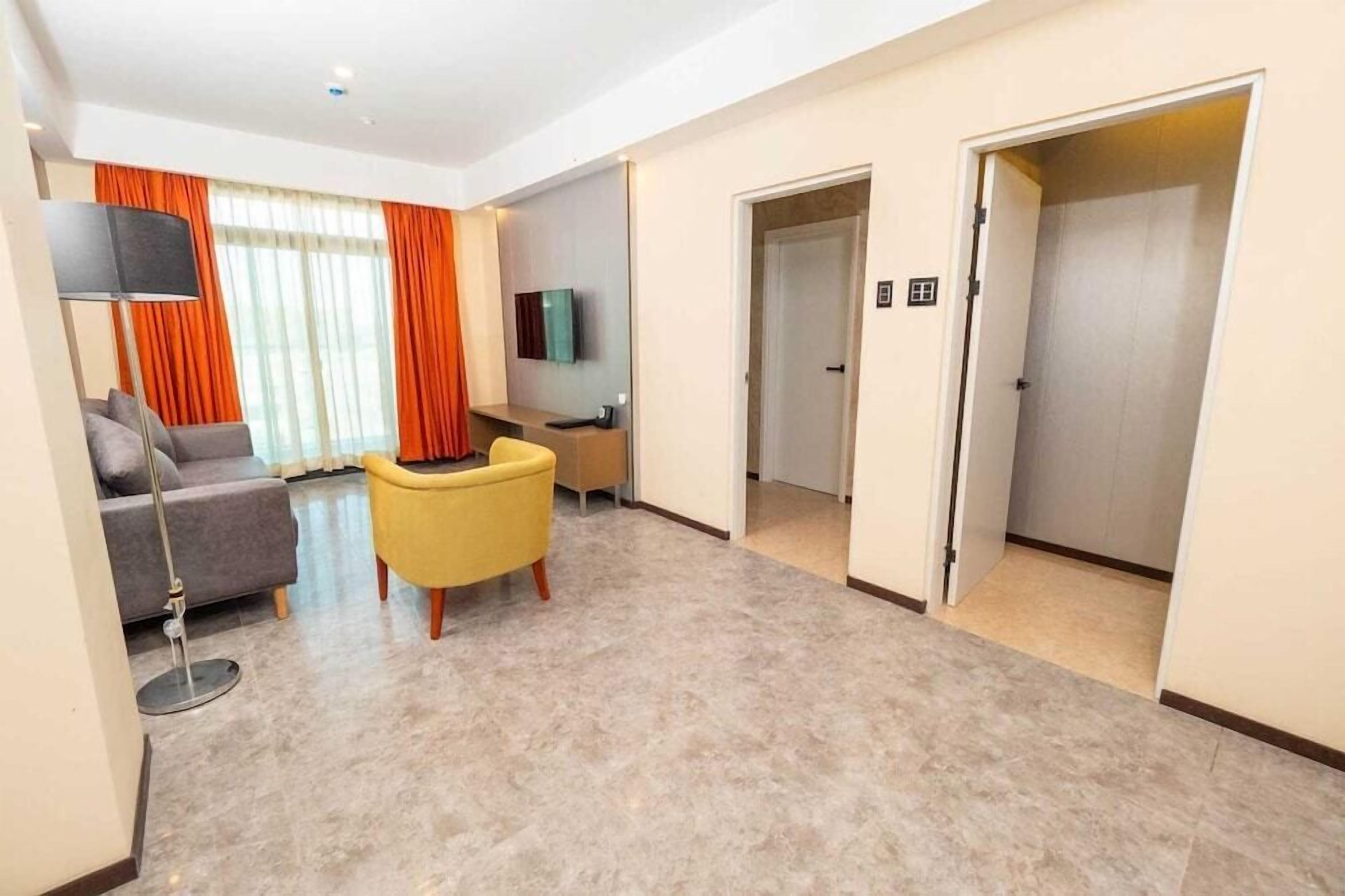 Quarto de hotel moderno com sofá, poltrona, televisão de tela plana e escrivaninha.