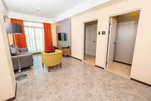 Una habitación de hotel moderna con sofá, sillón, televisor de pantalla plana y escritorio.