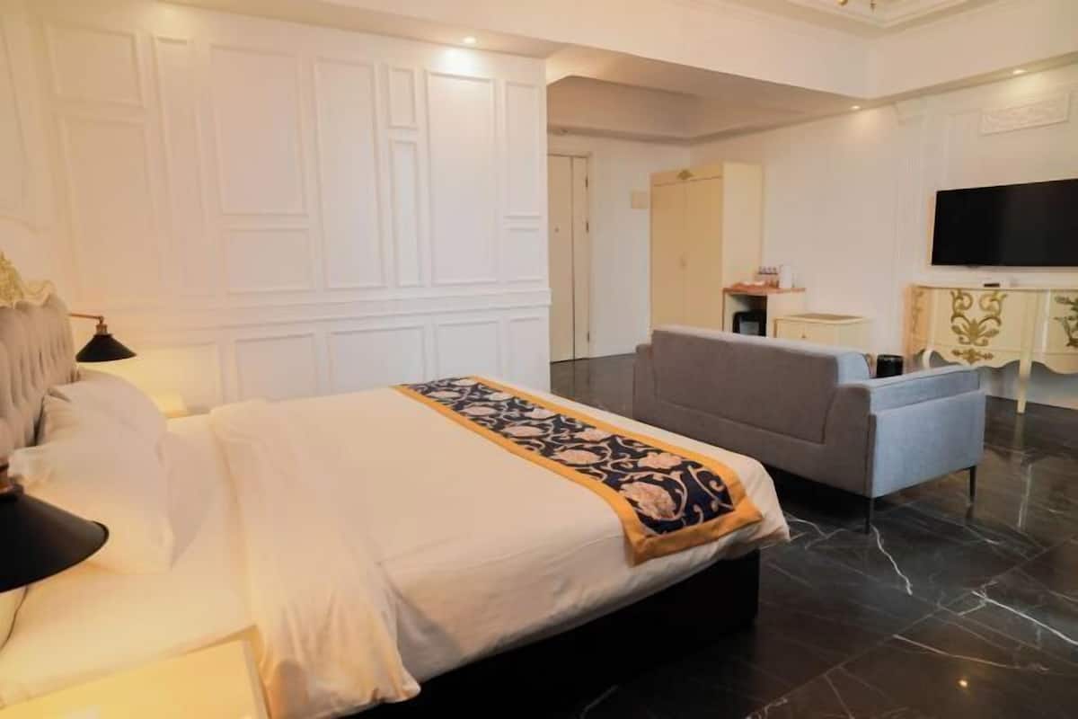 Une chambre d’hôtel avec un grand lit, un fauteuil gris, un téléviseur à écran plat et une petite table avec une lampe.