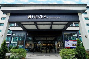 Une entrée d'hôtel moderne avec une façade en verre, une enseigne bien visible indiquant « HEVEA HOTEL & RESORT », et une banderole pour « DSND - Registro - Renforcement des capacités - GOUVERNANCE DES DONNÉES ».