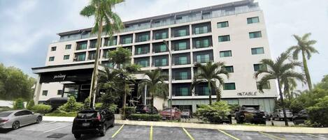 A multi-story hotel with a modern facade, a parking lot with several cars, and palm trees in the vicinity.