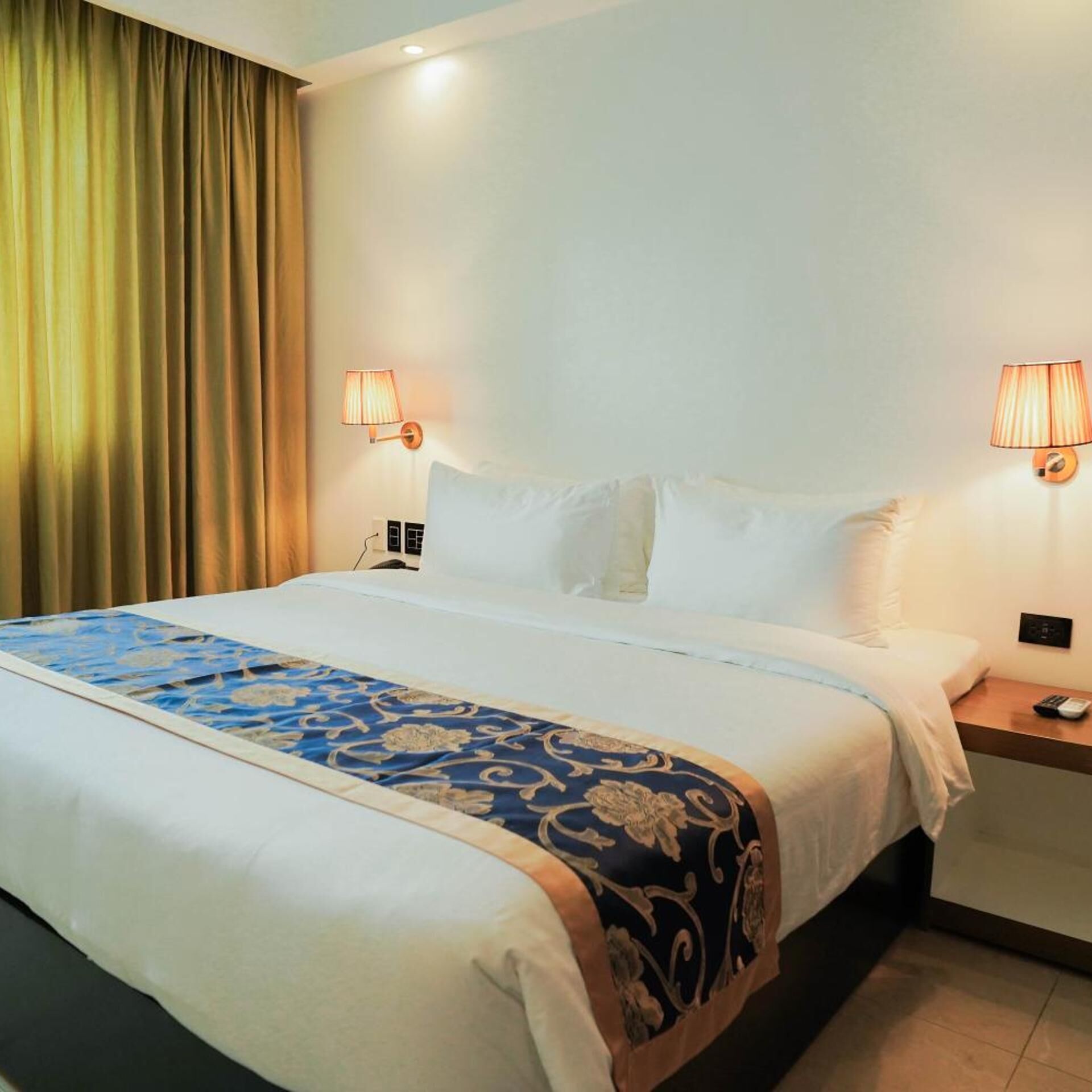 Een hotelkamer met een groot bed, twee bedlampjes, een nachtkastje en een gordijn.