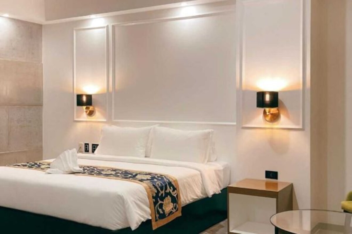 Une chambre d’hôtel avec un grand lit, deux lampes fixées au mur et une table de chevet.