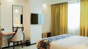 Ein Hotelzimmer mit Bett, Schreibtisch, Stuhl, Fernseher und einem Fenster mit Vorhängen.