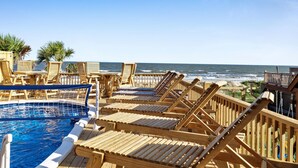 Une terrasse en bois avec des chaises longues et une piscine, offrant une vue sur l’océan.