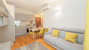 Un espacio habitable compacto con kitchenette, comedor y un sofá con cojines amarillos.