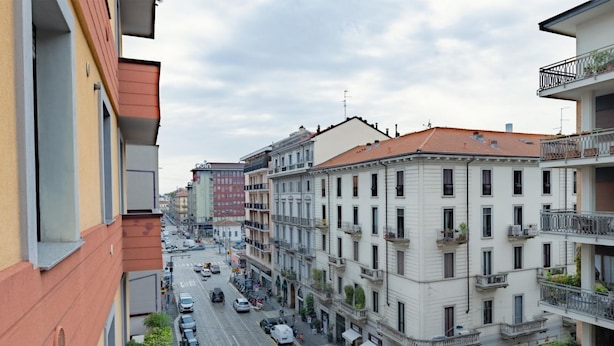 Un edificio de varios pisos con balcones, una calle delante y cielo despejado.
