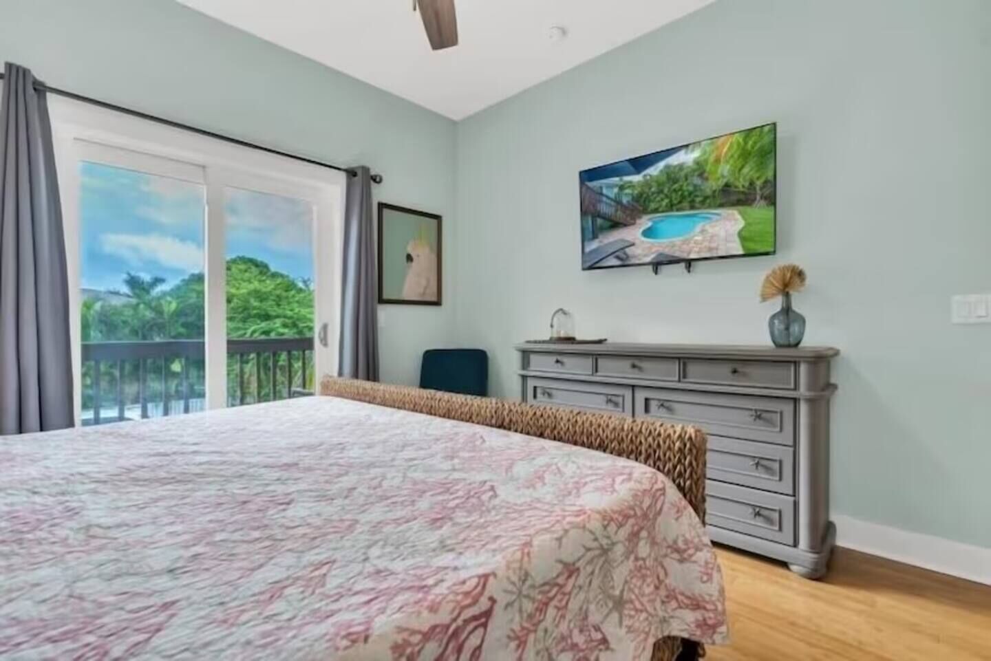 A bedroom with a large bed, a dresser, a painting, and a balcony with a view.
